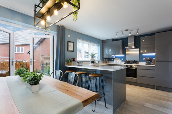 The modern kitchen of a new-build home with a breakfast bar and stools, chrome cabinetry and French doors to the garden