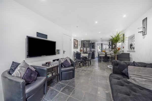 The modern open plan ground floor of a two bedroom cottage in Shoreham, Kent. The colour scheme is all grey with grey tiled flooring, dark grey sofa, armchair and soft furnishings, and grey kitchen furniture at the far end of the room.