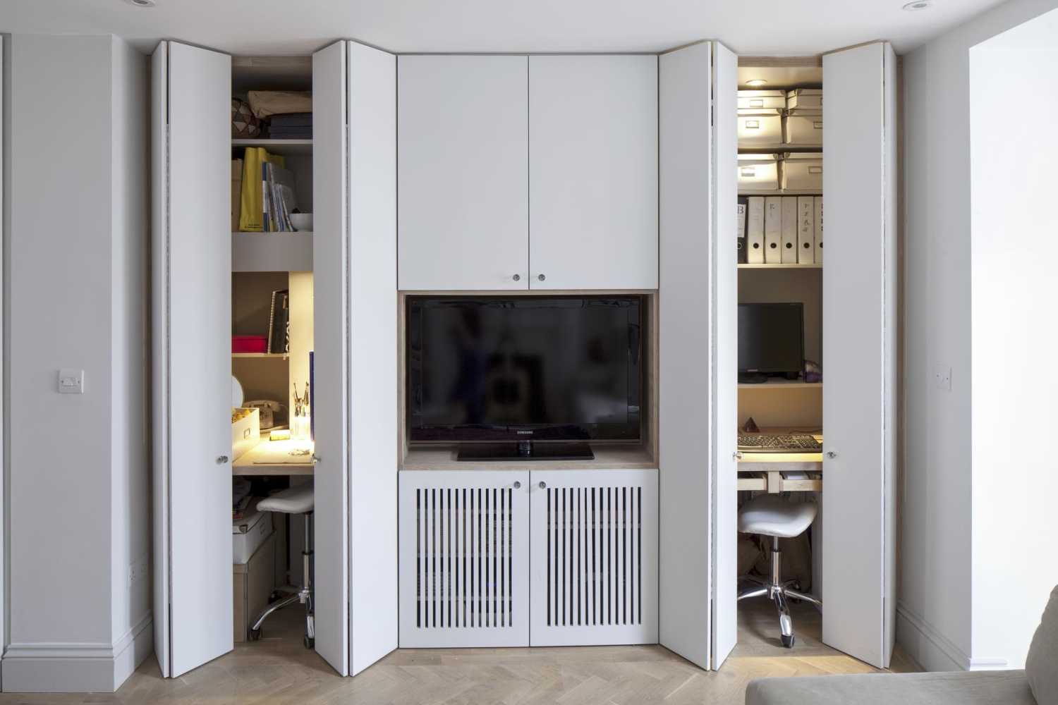 White cupboard doors opening to reveal hidden desks and shelves on either side of a TV