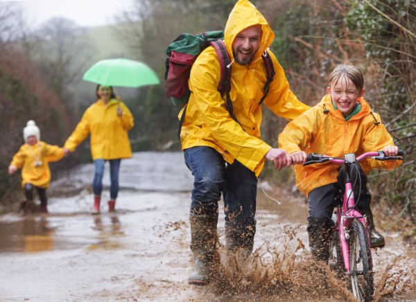 A family in yellow raincoats riding bikes and walking in the rain through a woodland