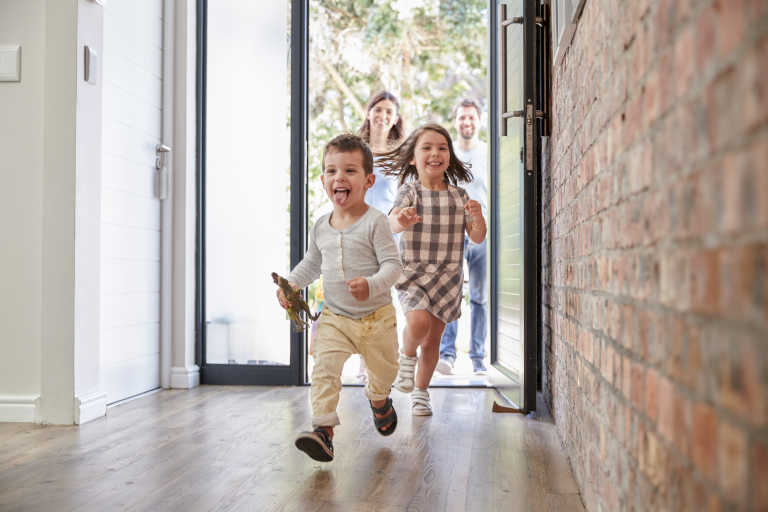 Small children running through the front door of their home as their parents follow behind
