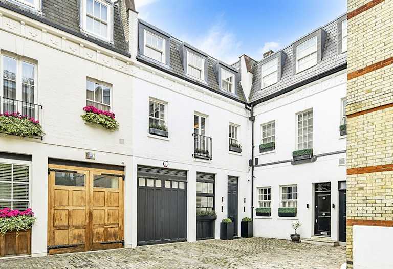 A white terraced mews house with black trim including a black garage door, black front door and black railings outside the windows.