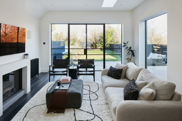 A stylish lounge extension with neutral decor, a modern fireplace and full-height glass doors leading to a large lawned garden