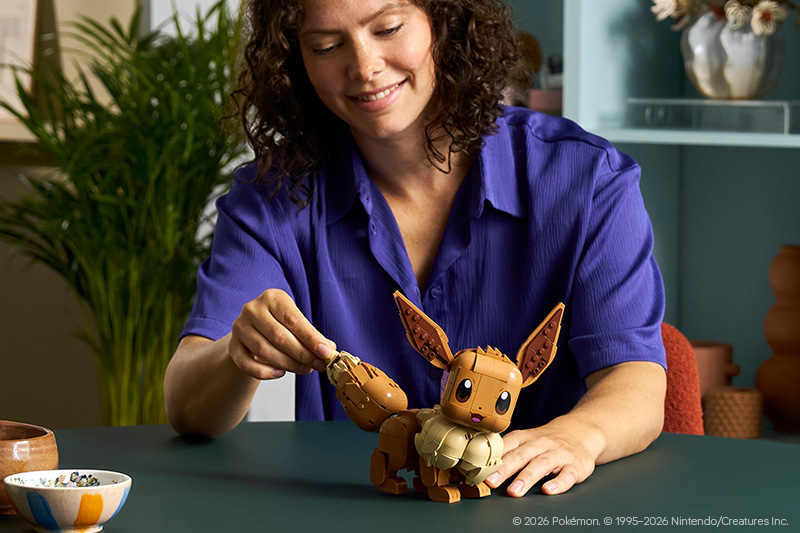 A lady building the LEGO Pokémon 72151 Eevee Set for Adults on a table in a room.