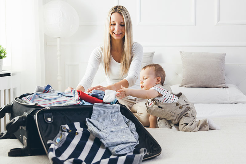 A mom packing a suitcase with her baby on a bed in a bedroom.