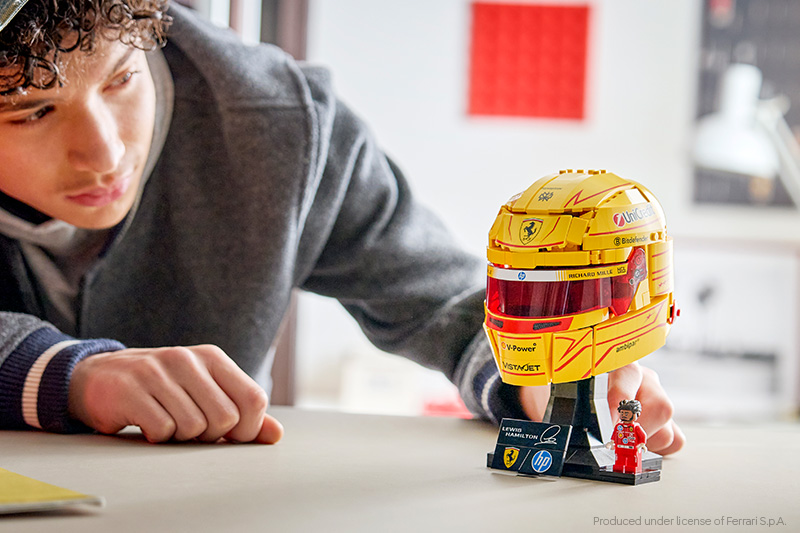 A man building the LEGO Editions 43022 Scuderia Ferrari HP Lewis Hamilton Helmet Set on a tabletop.