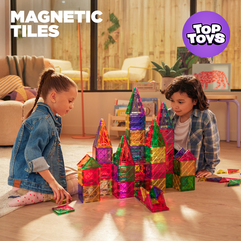 Two kids playing with the Magnetic Tiles Building Sets on the floor in a room.