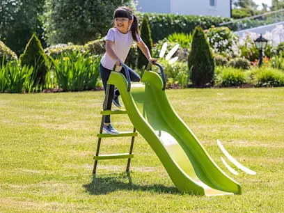 A child climbing up the steps on the 5.8ft Wavy Slide on a green garden lawn. 