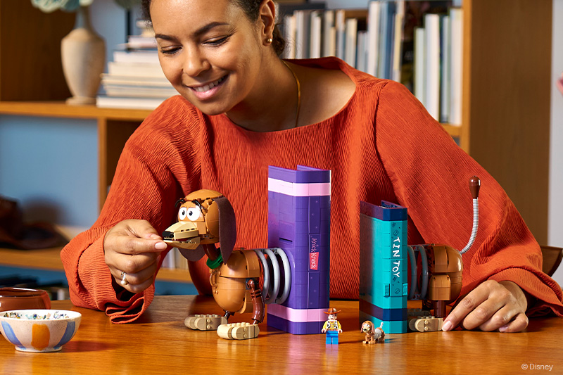 A lady building the LEGO Disney 43301 Toy Story Slinky Dog Bookends Set for Adults on a tabletop in a room.