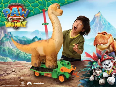 PAW Patrol: The Dino Movie promotional image showing a child beside a large 76 cm dinosaur toy mounted on a green vehicle, with dinosaur characters and PAW Patrol pups in a prehistoric landscape.