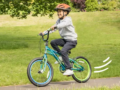A kid riding on the 18 Inch Glitch Bike Metallic Blue on a garden path.