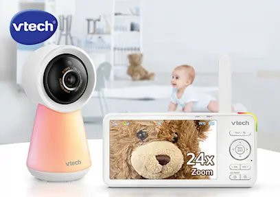 The VTech RM5756HD Smart Wi-Fi Video Baby Monitor with 5 Inch Screen on a tabletop with a baby crawling on the floor in the background.