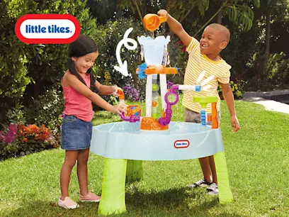 Two children joyfully play with a Little Tikes water table in a sunny garden. The boy pours water, while the girl interacts with toys.