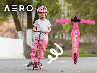 A young child in pink helmet and pants rides a pink Aero scooter on a park path.