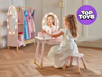 A kid sitting at the Dimples Light Up Wooden Vanity Table with the Dress Up Rack at the back of the room.
