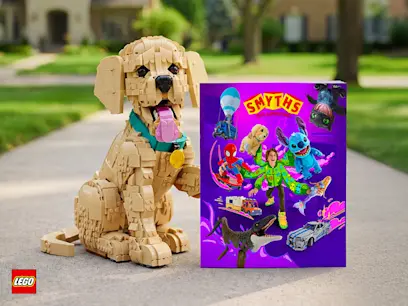 The LEGO Icons 11384 Golden Retriever Puppy Set for Adults sitting beside the Smyths Toys Catalogue on a footpath in a leafy neighboorhood.