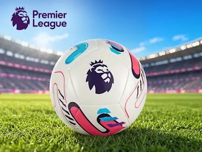 Premier League Size 5 football with the league lion logo and colourful graphics, resting on grass in a sunlit football stadium. The Premier League logo appears in the upper-left corner.