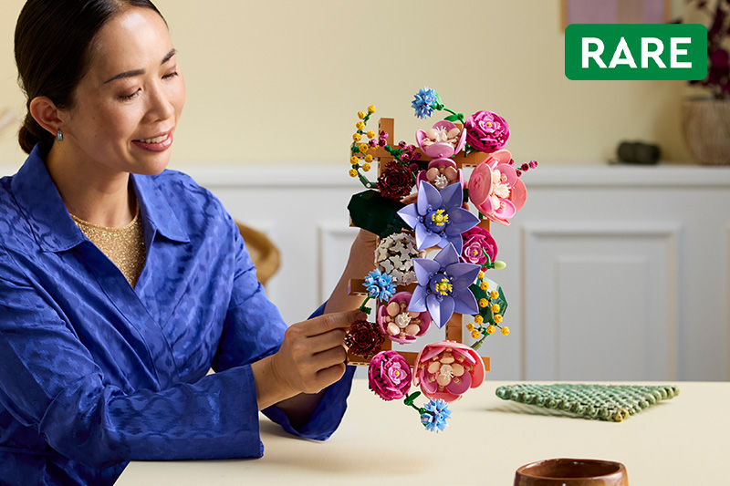 A woman fixing and building the LEGO Botanicals 11503 Flower Wall Set for Adults on a table in a living room.