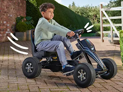 A young boy drives a black go-kart along a paved garden path.