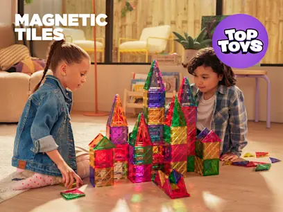 Two kids playing with the Magnetic Tiles Building Sets on the floor in a room.