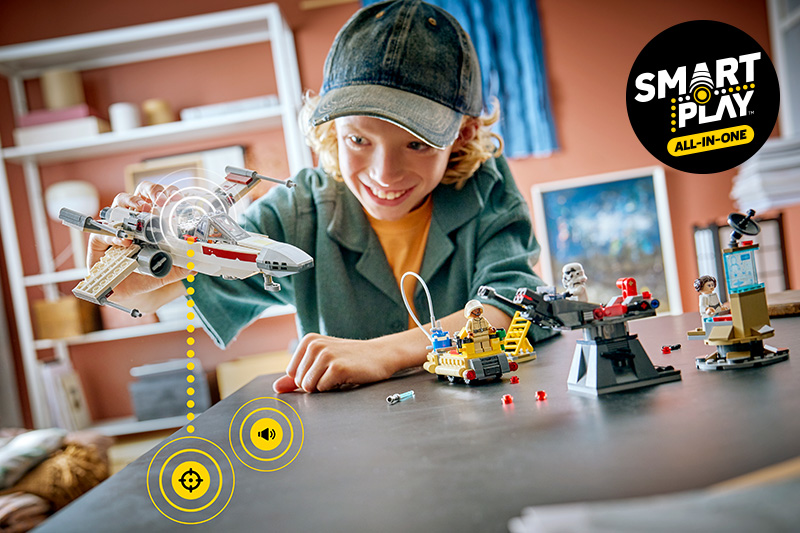 A kid building the LEGO Star Wars 75423 SMART Play: Luke's Red Five X-Wing Set on a tabletop in a room