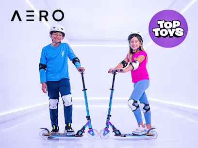 A boy and girl standing on the Aero Neo Chrome Kick Scooter while wearing helmets in a lit up room.