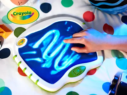 A child's hand draws on a glowing blue Crayola tablet on a polka dot surface. 
