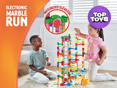 Children playing with a colourful electronic marble run toy indoors by a window.