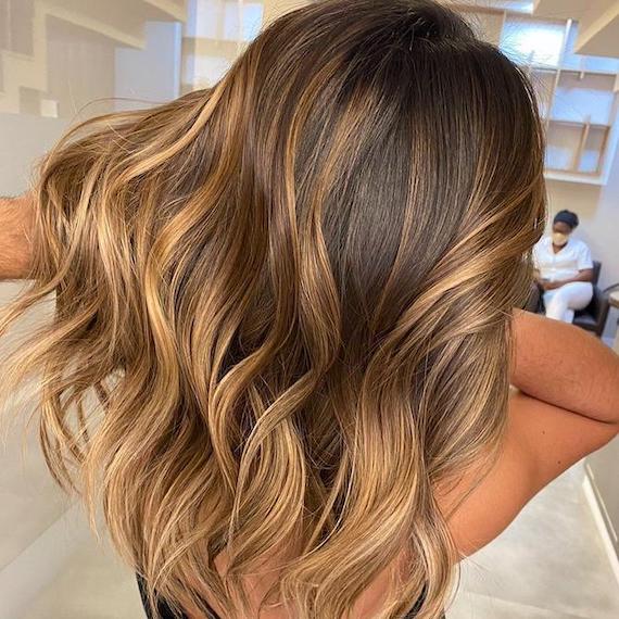 Caramel balayage with shadow root in loose waves with sunbeam lighting