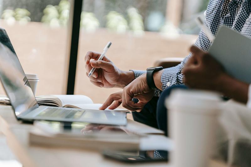 Man taking notes on a laptop with pen in hand.