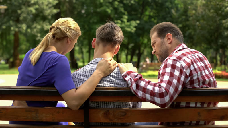 A young man sits with his parents in a park