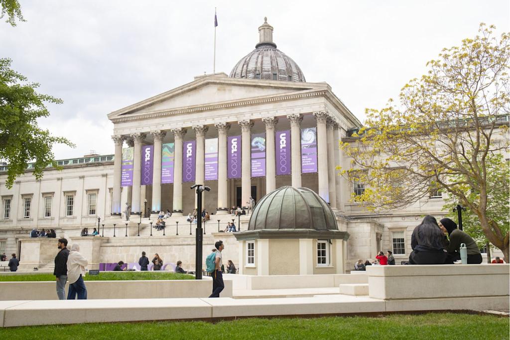 UCL's main quad - a large sandstone building with columns and steps leading to the entrance and students milling around outside.