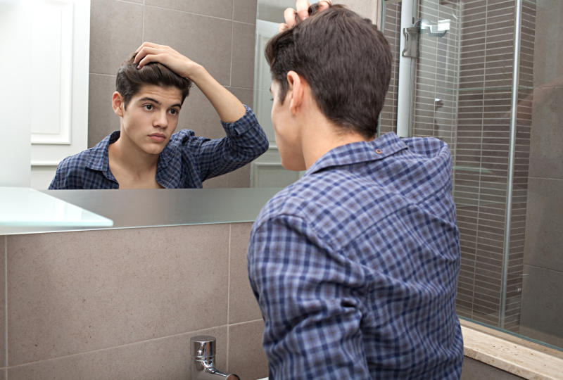 A young boy looks at his appearance in a mirror