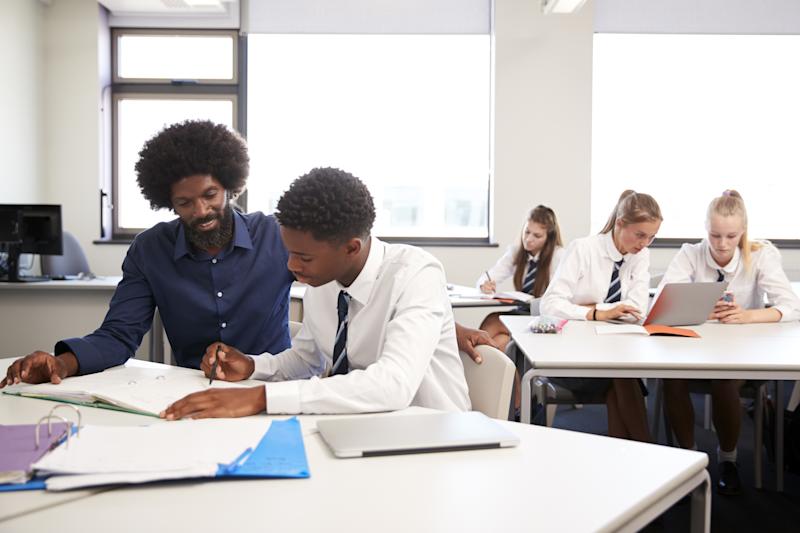 High School Tutor Giving Uniformed Male Student One To One Tuition At Desk In Classroom