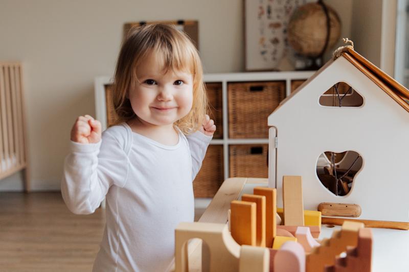 young child smiles at camera with pride and hands raised to side with toys in front of them.