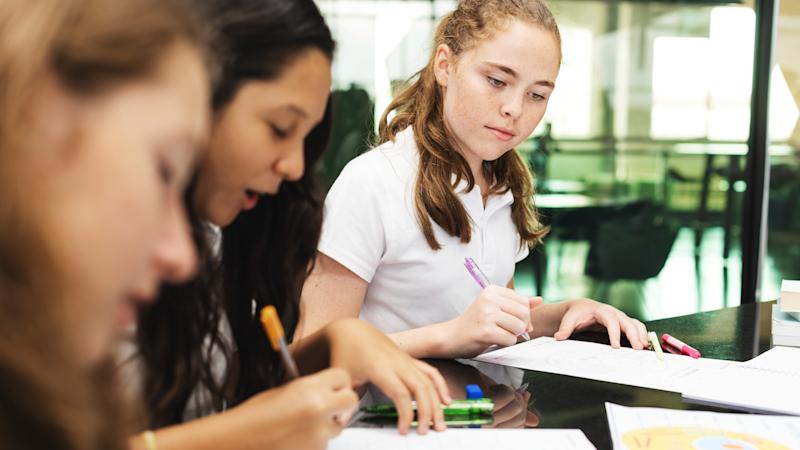 Three secondary school children looking down at their work with pens in their hands.
