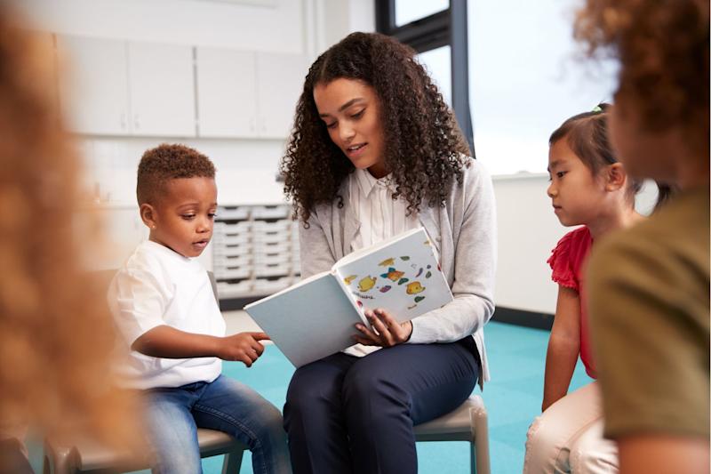 Teacher reading a book to children seated in a circle, with children on either side in focus.