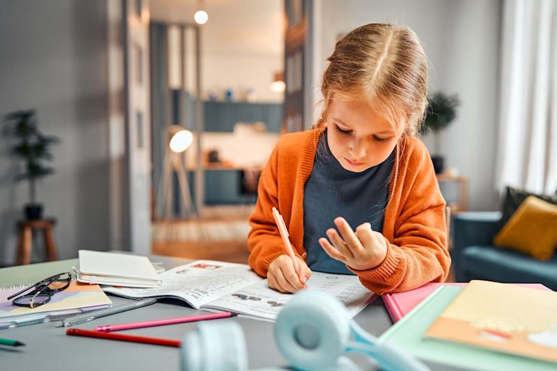 Photograph of a young girl counting on her fingers and writing in a workbook.