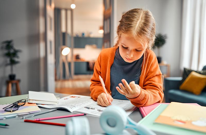 Photograph of a young girl counting on her fingers and writing in a workbook.