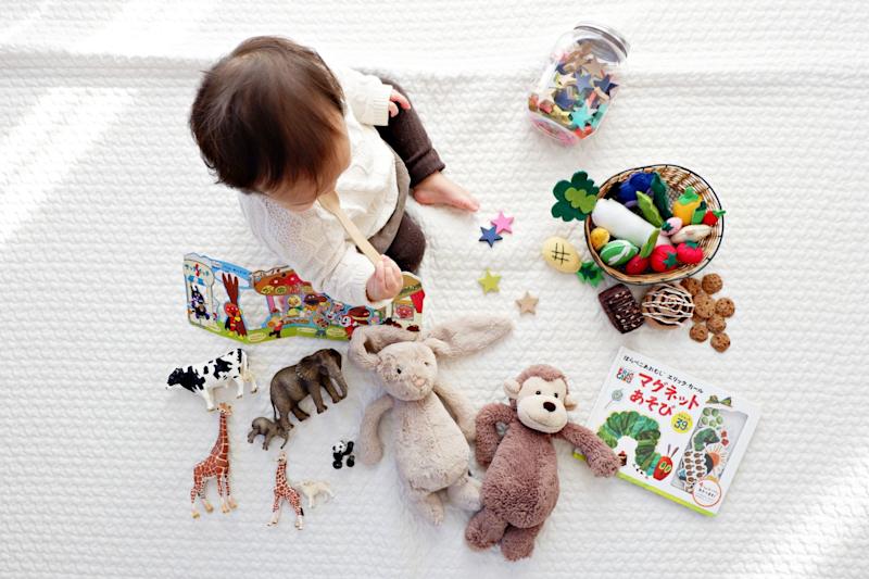 Photographed from above, a baby sitting on floor playing with toys.