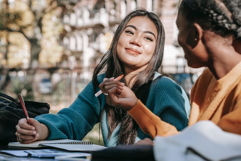 women smiling at each other while appearing to be studying in the outdoors