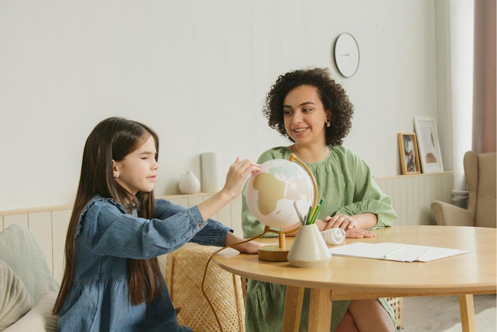 Photograph of a therapist sitting at a table with a girl, who is pointing to a country on a globe.