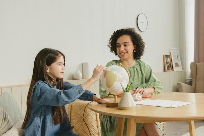 Photograph of a therapist sitting at a table with a girl, who is pointing to a country on a globe.