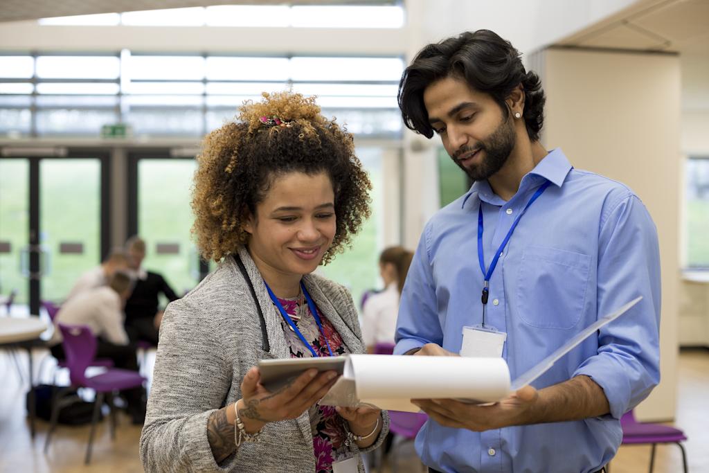Two school teachers holding some paperwork in front of them and discussing it together.