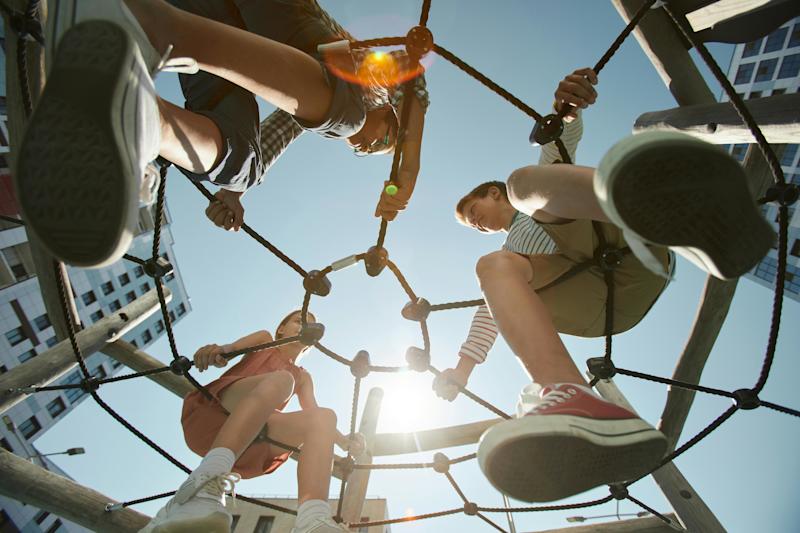 Upward view of three children sitting on swings at a playground.