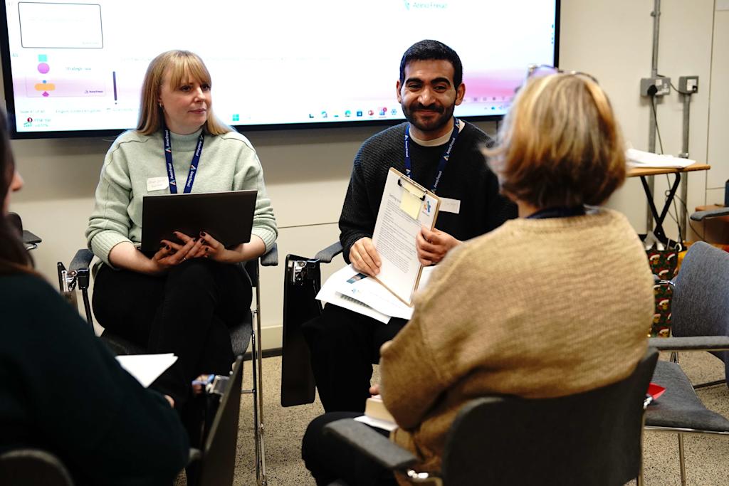 Three Anna Freud students in a seminar, with a male student in the middle smiling at someone opposite him.