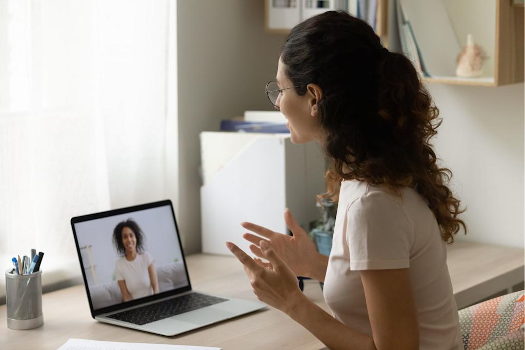Woman sitting at a desk at home, speaking with another woman via a laptop.