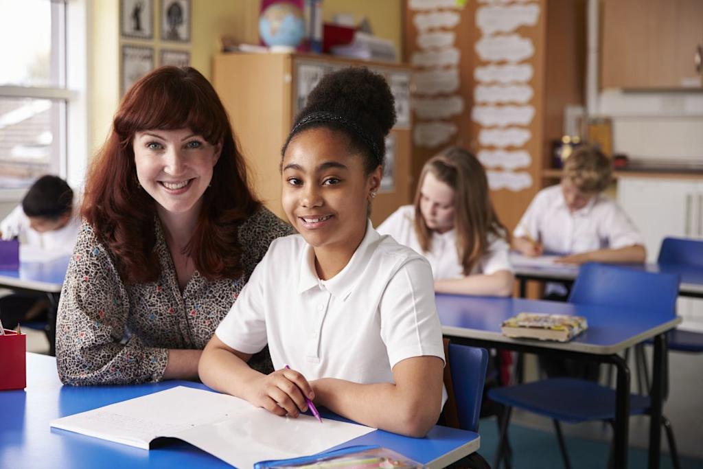 Primary school teacher and pupil in a classroom smiling towards the camera.