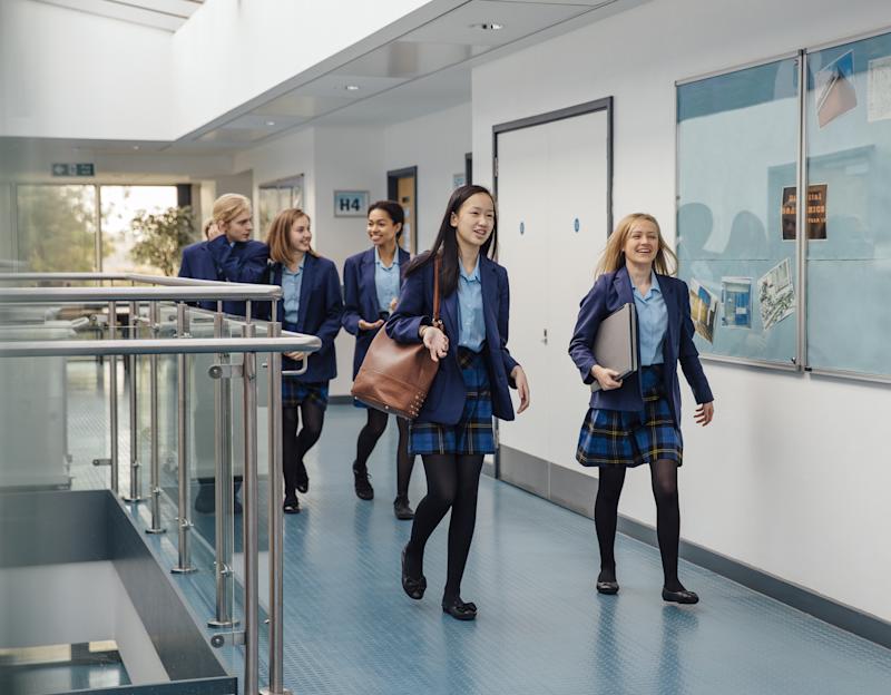 Group of students are walking down the school corridor together wearing uniform.