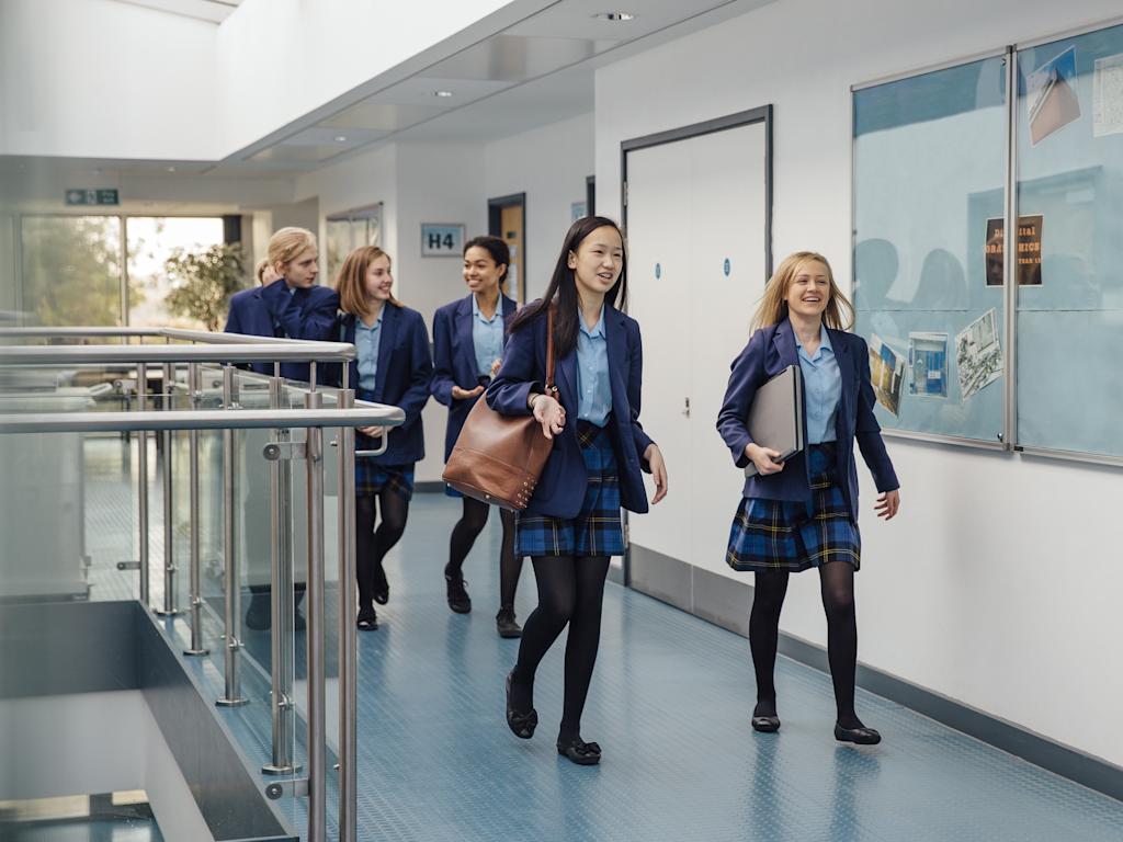 Group of students are walking down the school corridor together wearing uniform.